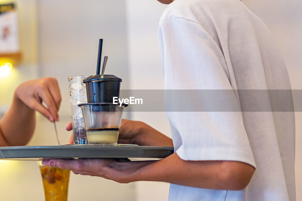 food and drink, adult, drink, one person, holding, refreshment, indoors, midsection, women, household equipment, young adult, food, lifestyles, coffee, kitchen appliance, glass, cup, business, drinking glass, domestic room, home appliance, standing, hand, focus on foreground, kitchen, drinking, occupation, coffee cup, mug, casual clothing, domestic life