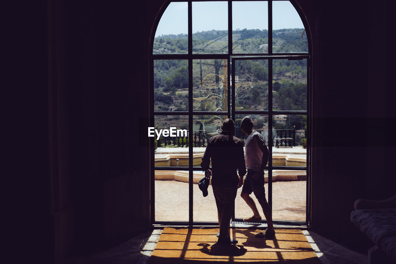 REAR VIEW OF COUPLE STANDING AGAINST WINDOW