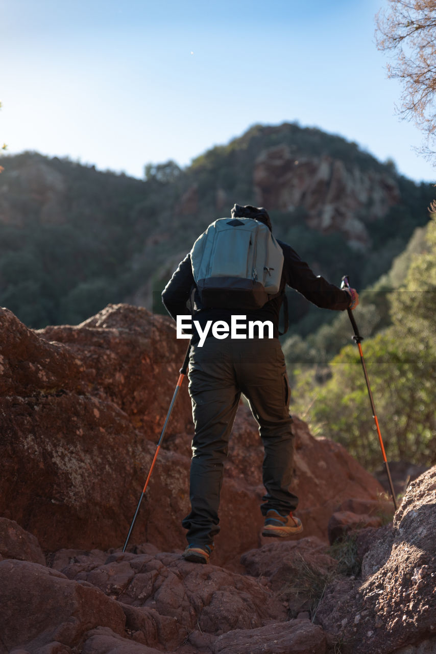 Middle-aged man climbs the mountain in the garraf natural park, supported by hiking poles.