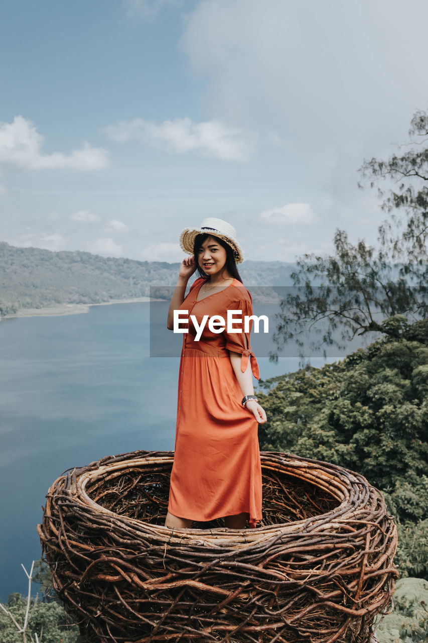 Portrait of smiling young woman standing against sky