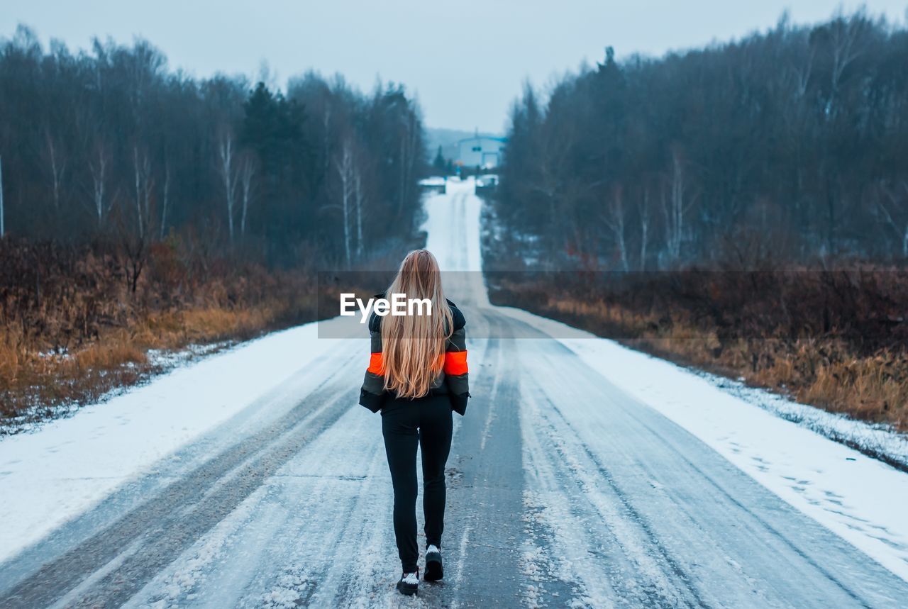 Rear view of woman walking on snow covered road