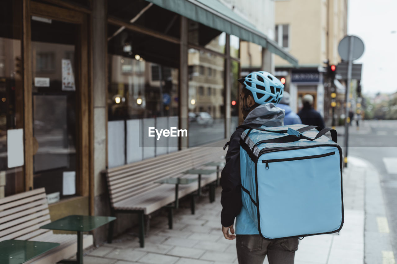 Rear view deliver man with backpack on sidewalk