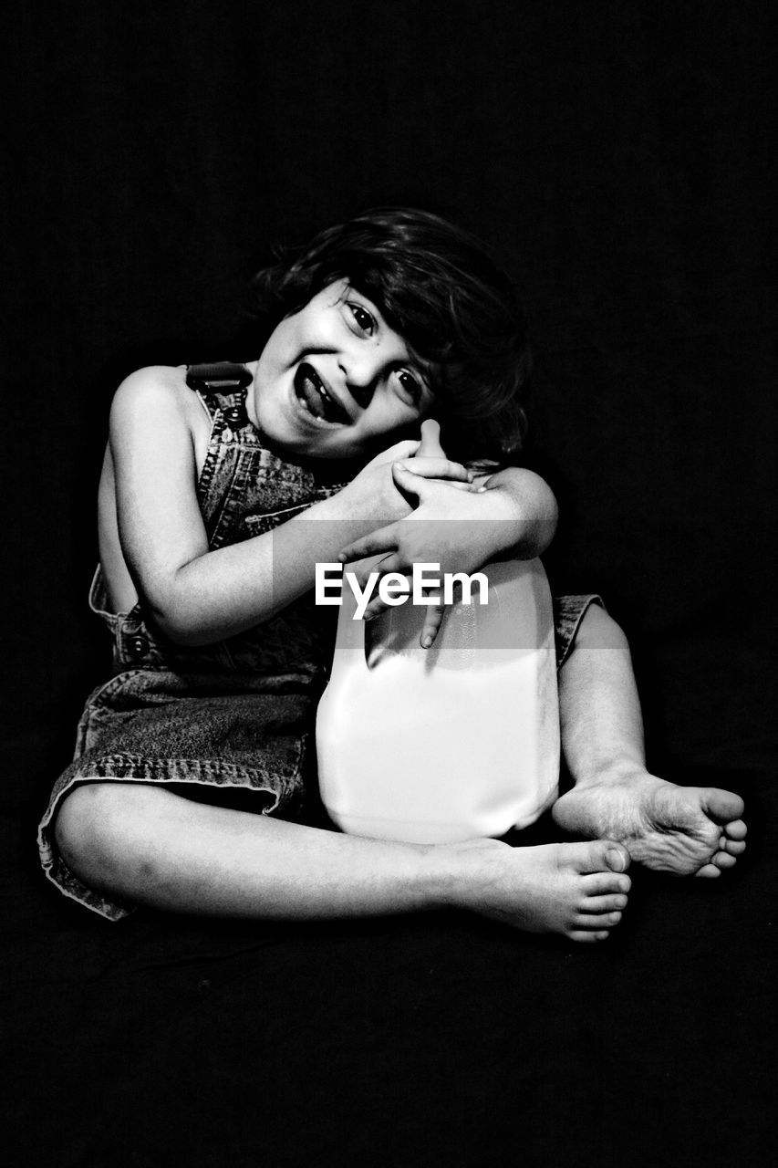 Full length of smiling girl holding container with milk against black background