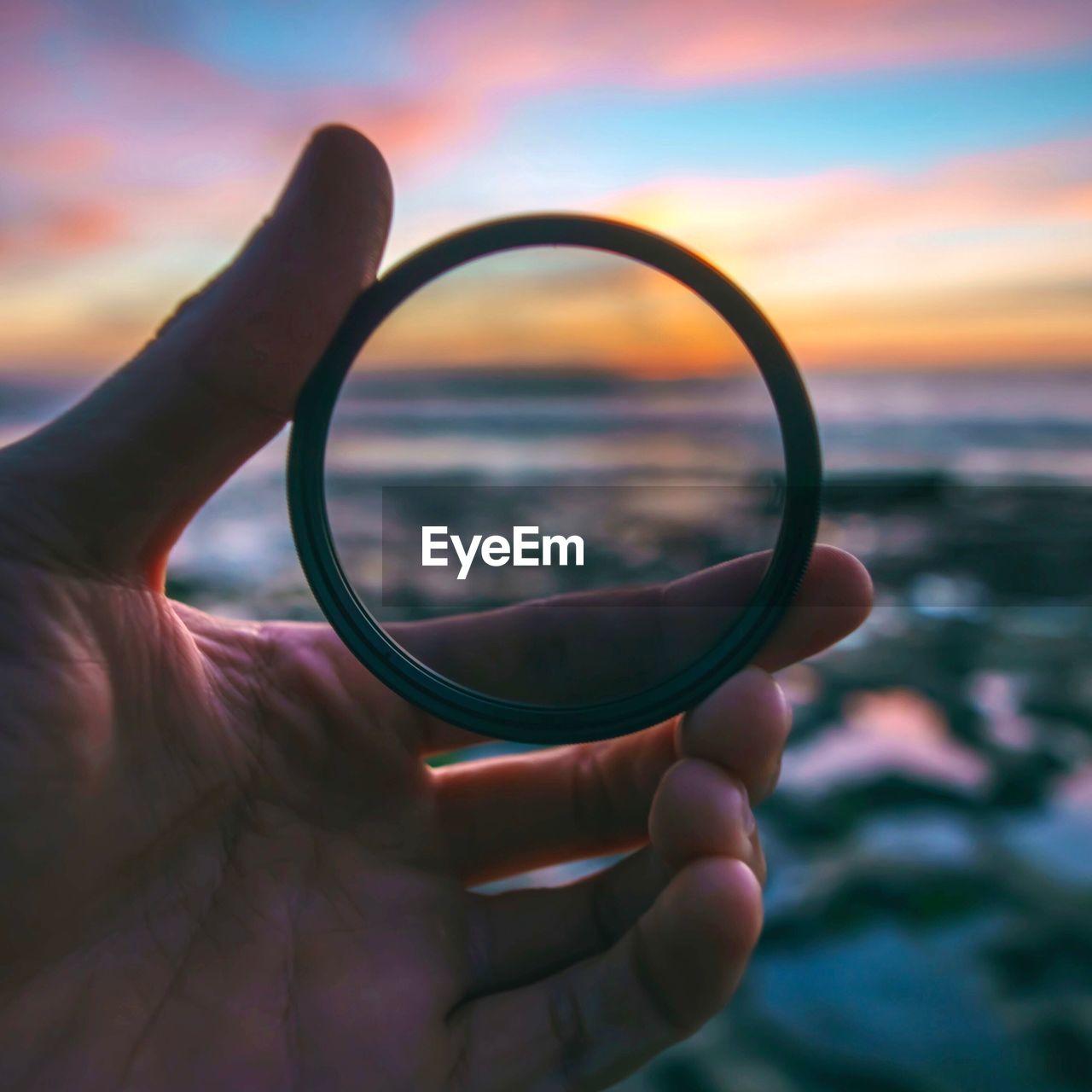 Cropped hand holding bangle against cloudy sky during sunset