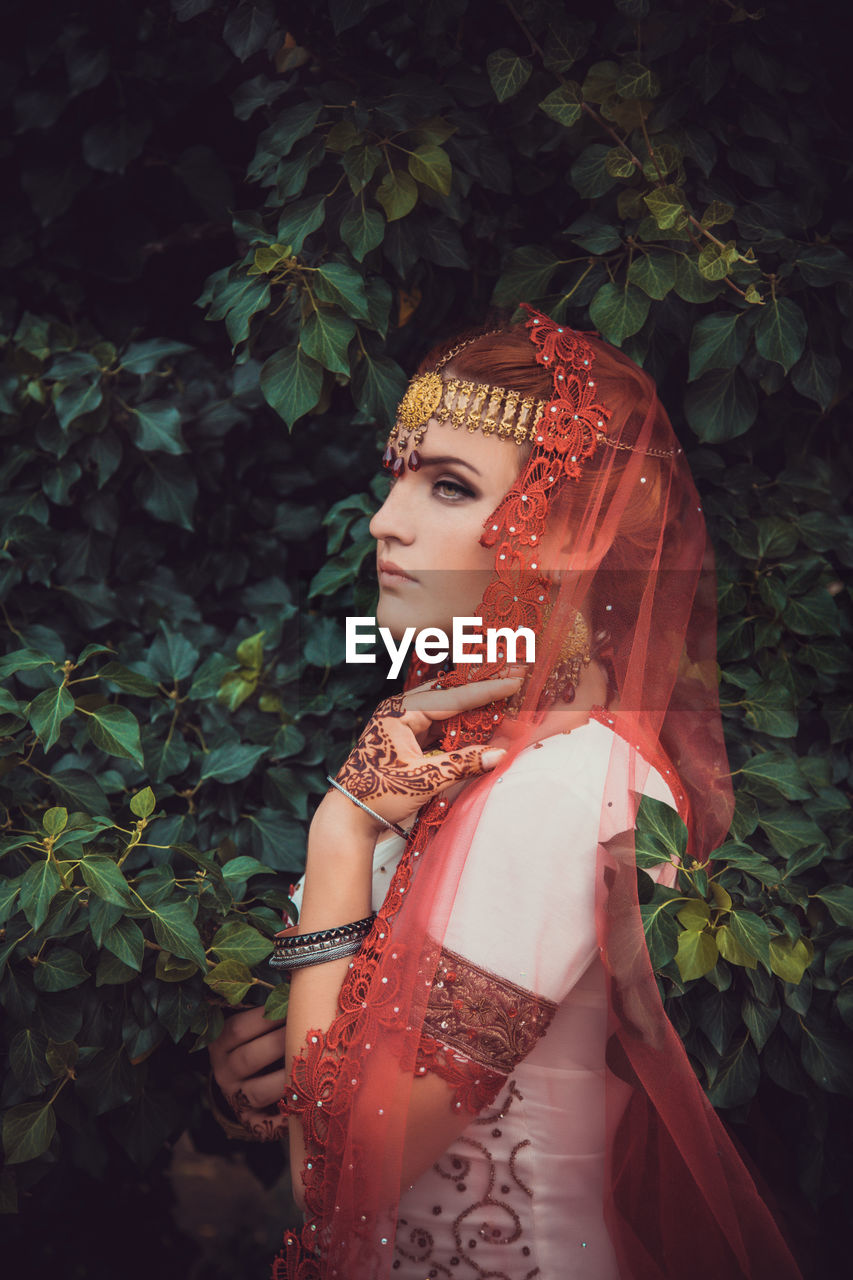 Portrait of young woman standing against plants