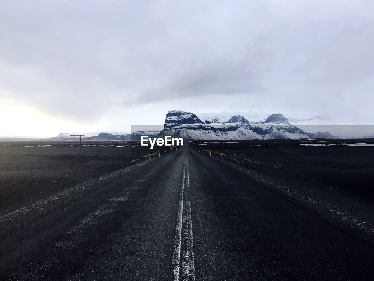 Road leading towards snowcapped mountain against cloudy sky