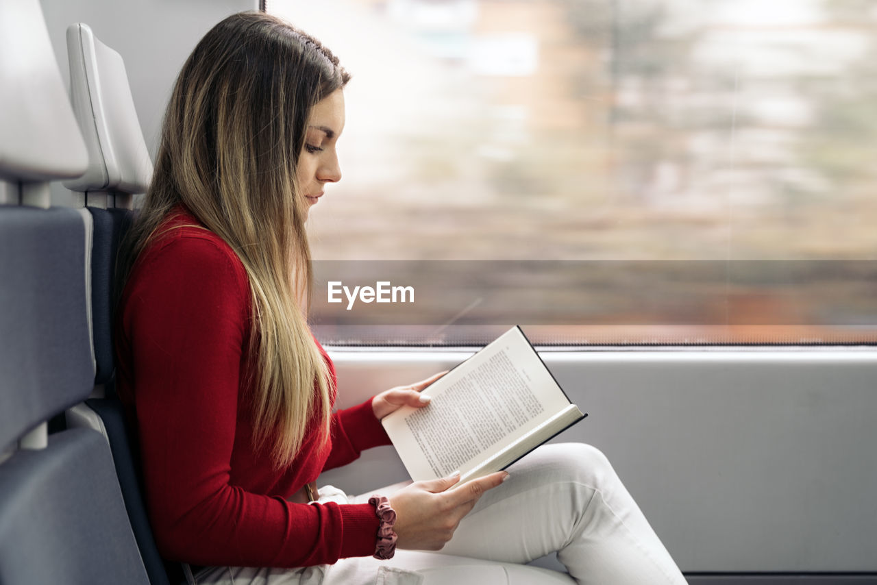 WOMAN HOLDING BOOK WHILE SITTING ON SEAT IN SHELF