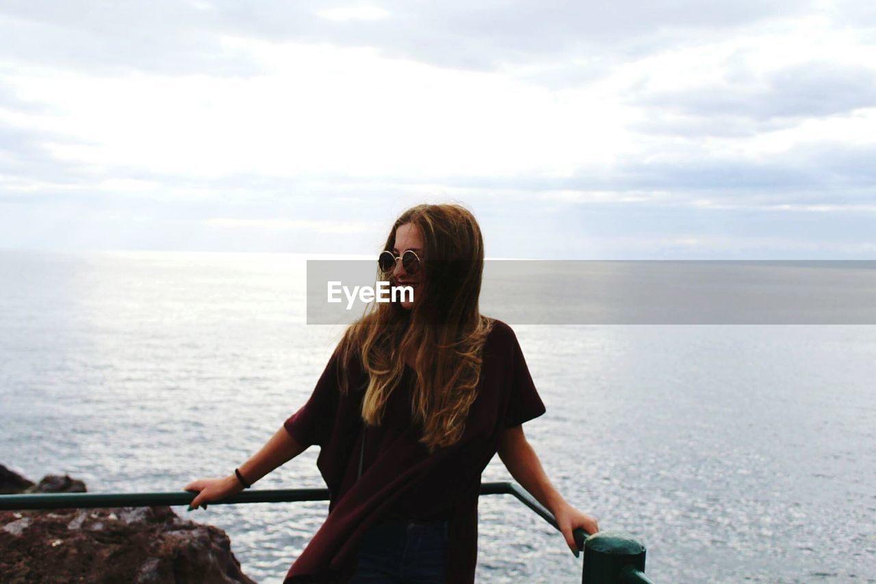 Young woman leaning on railing against sea