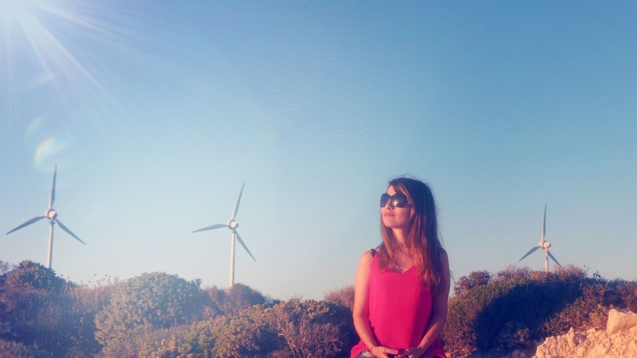 Young woman sitting against clear sky on sunny day