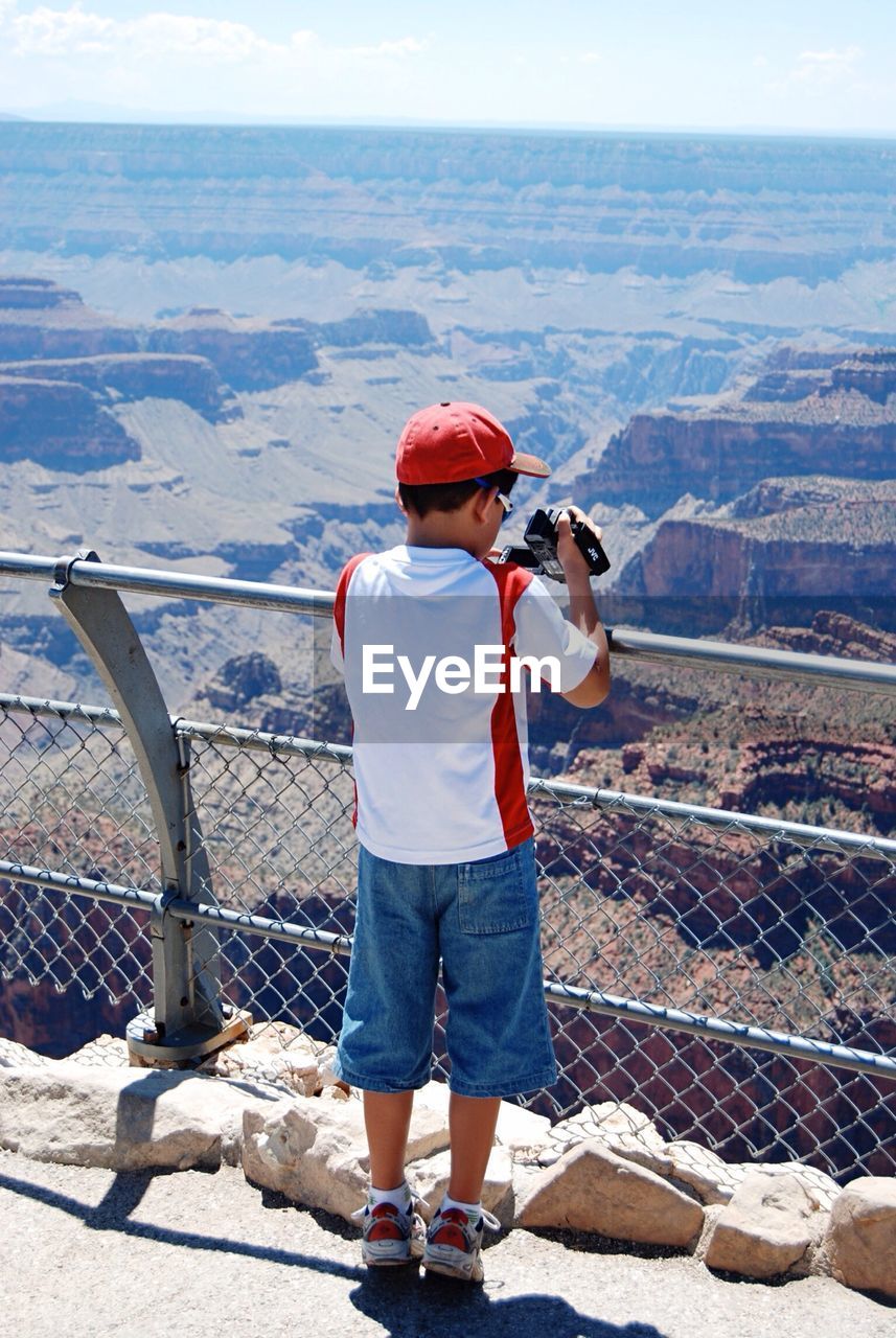 Rear view of boy filming grand canyon with video camera