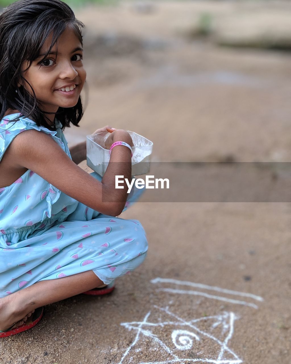 Portrait of smiling girl making rangoli while sitting on land
