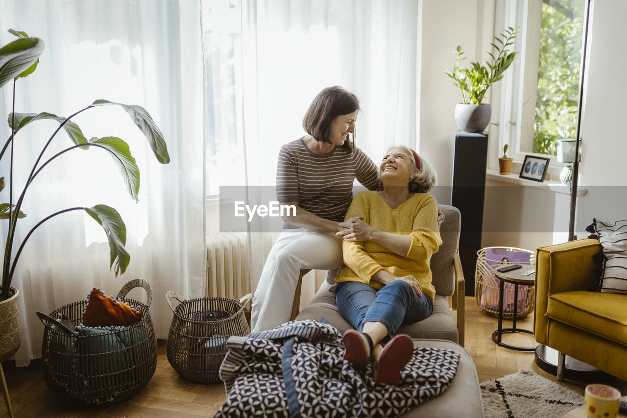 Smiling mature woman spending leisure time mother-in-law sitting on chair in living room at home