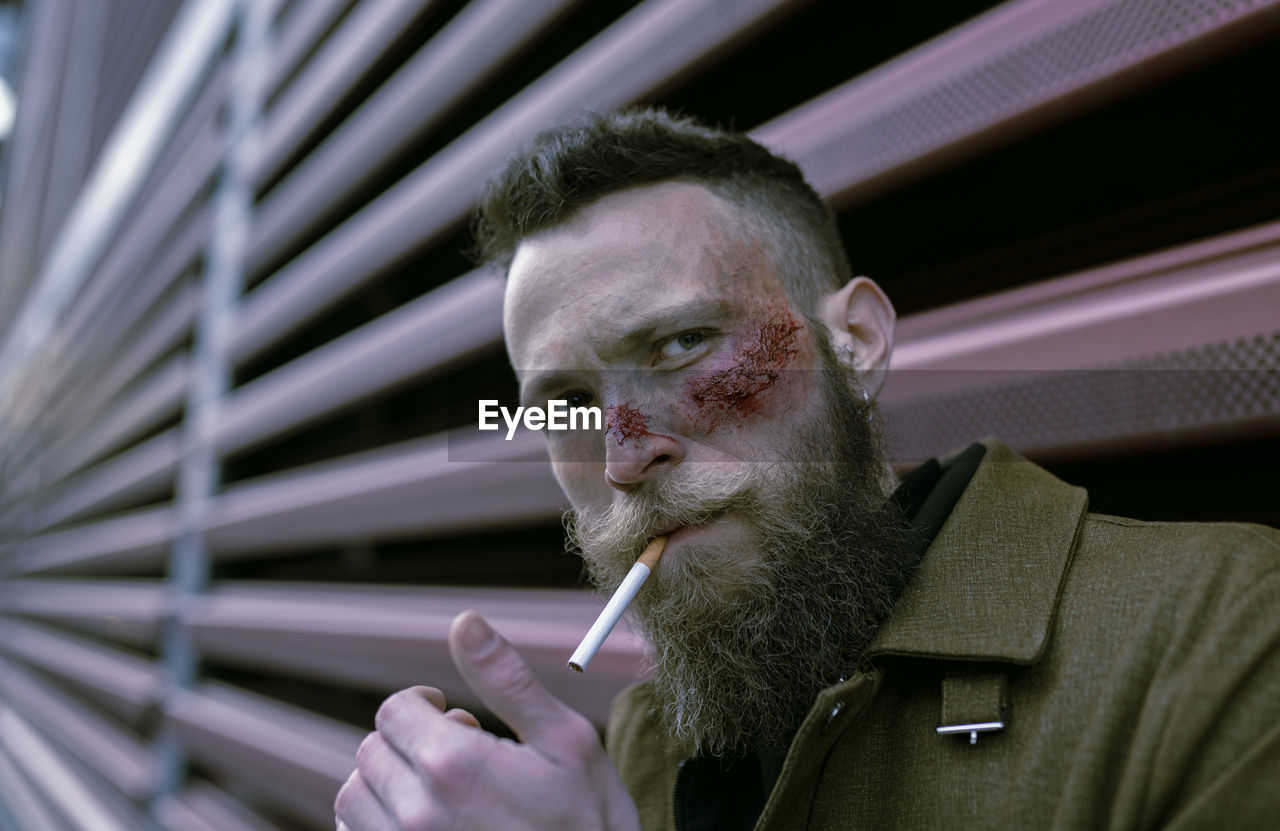 Hipster man with beard and cinema makeup smoking a cigarette