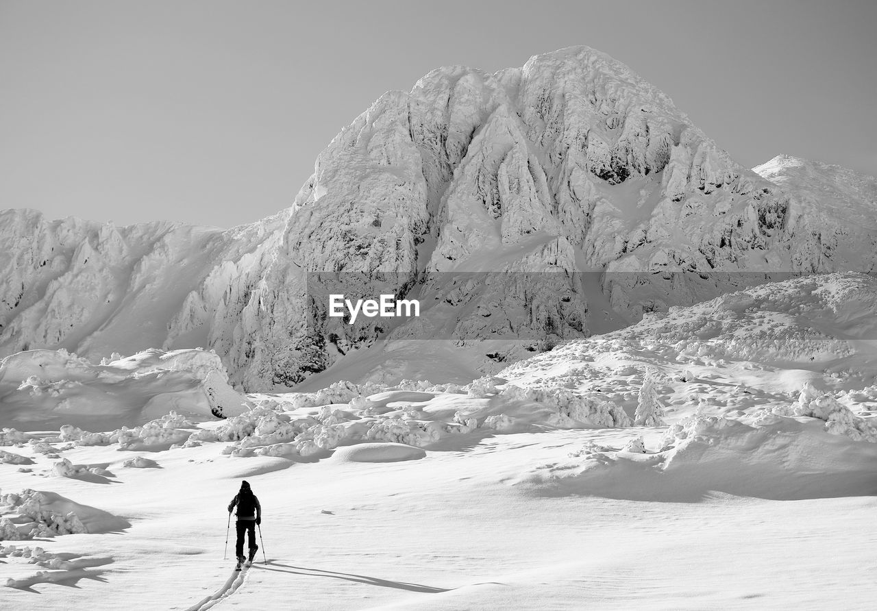 MAN WALKING ON SNOWCAPPED MOUNTAIN AGAINST SKY