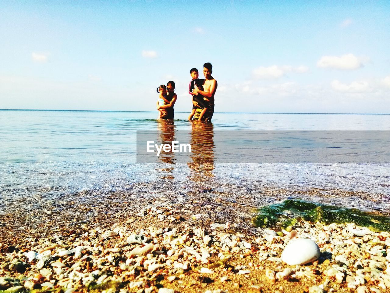 Family standing in sea against sky