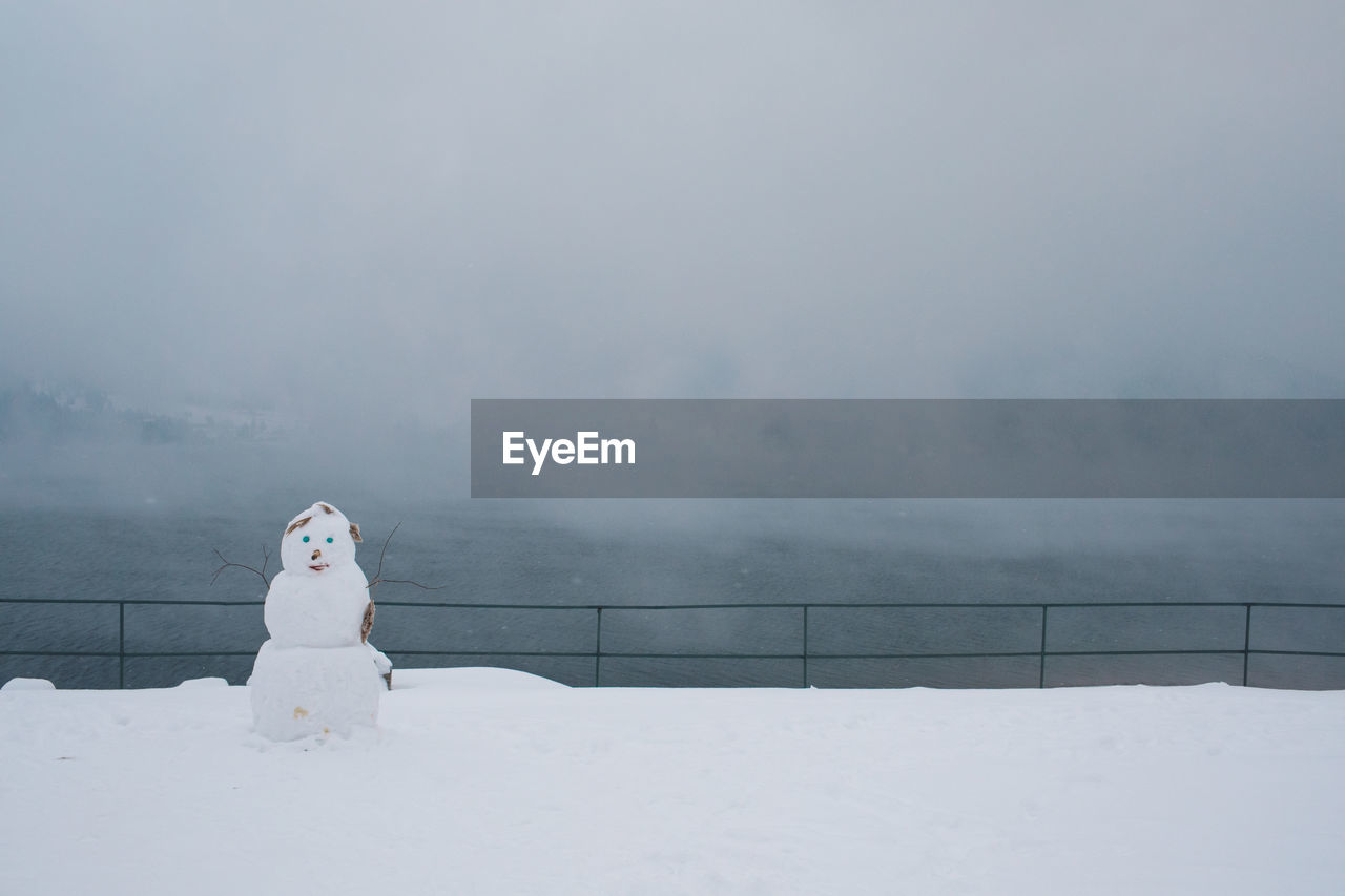 Snowman on snow covered field by railing during foggy weather