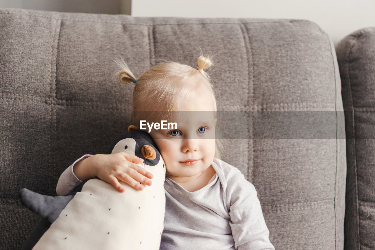 Portrait of a child on a couch with a toy penguin