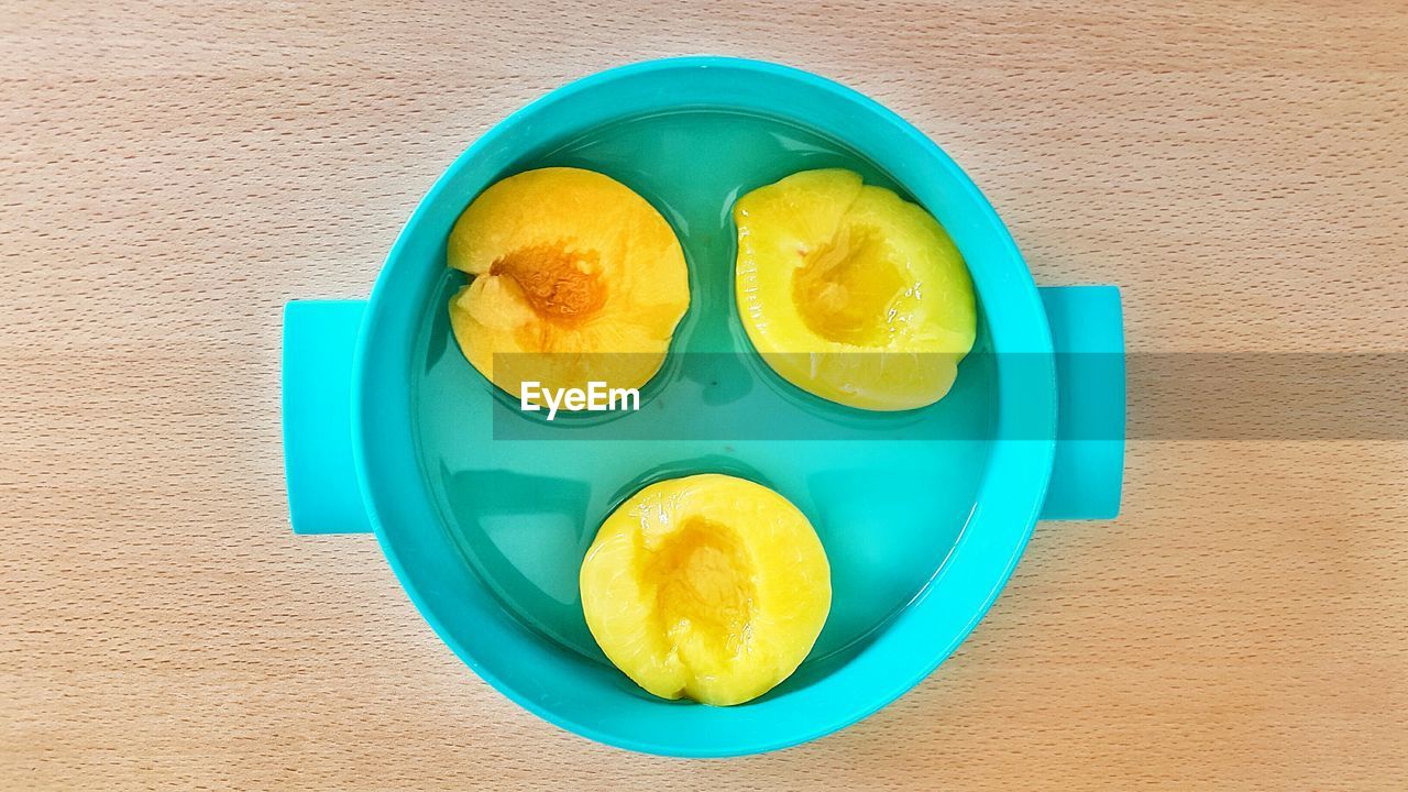 Directly above shot of wet peaches in container on wooden table