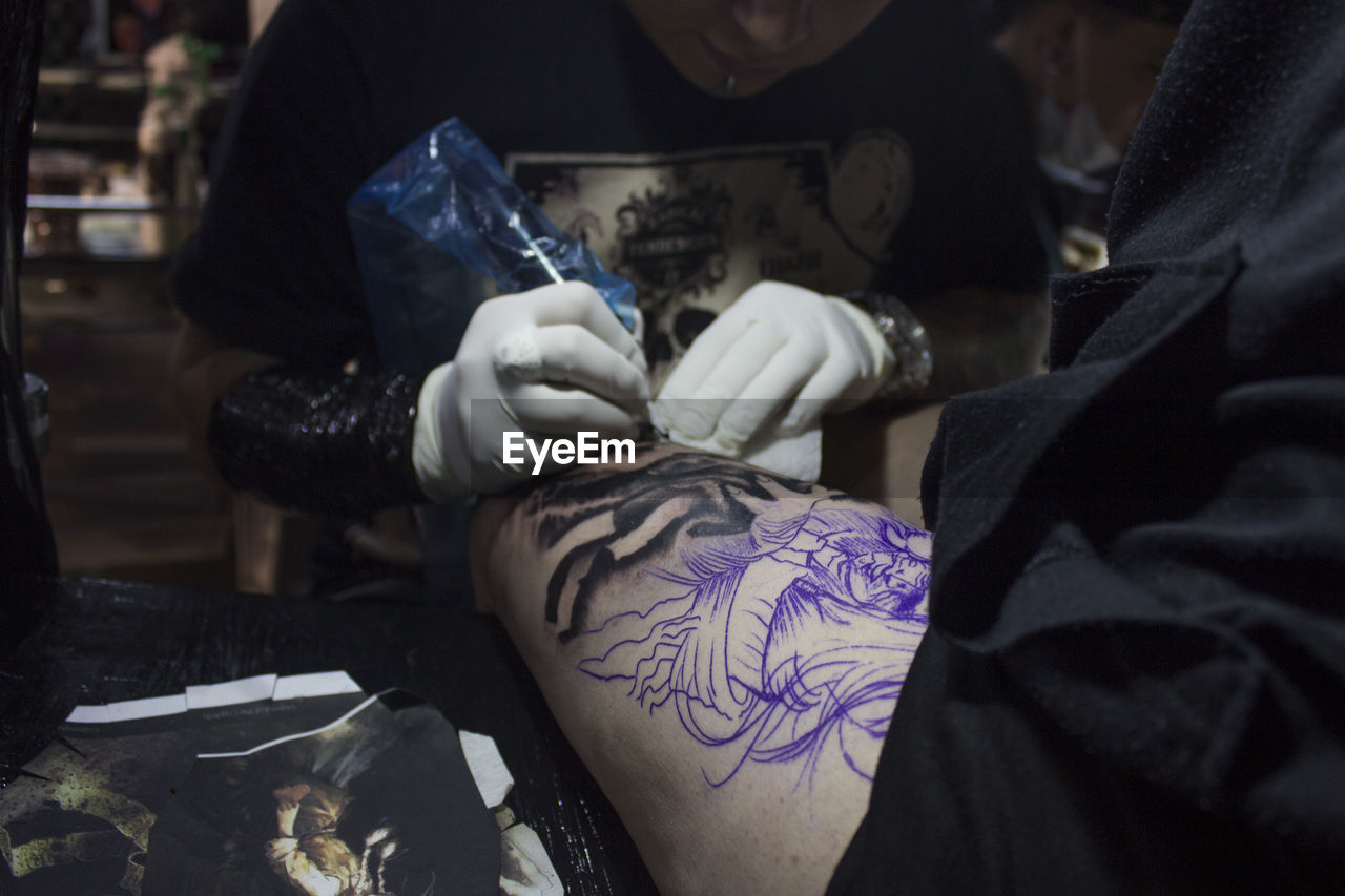 Artist tattooing on thigh of woman at studio