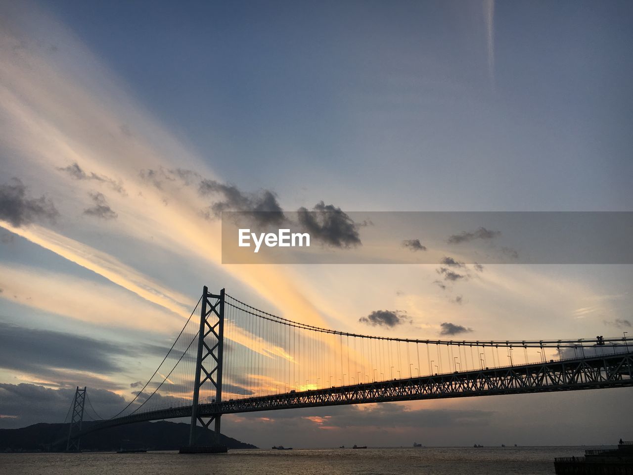 Suspension bridge over sea against sky during sunset