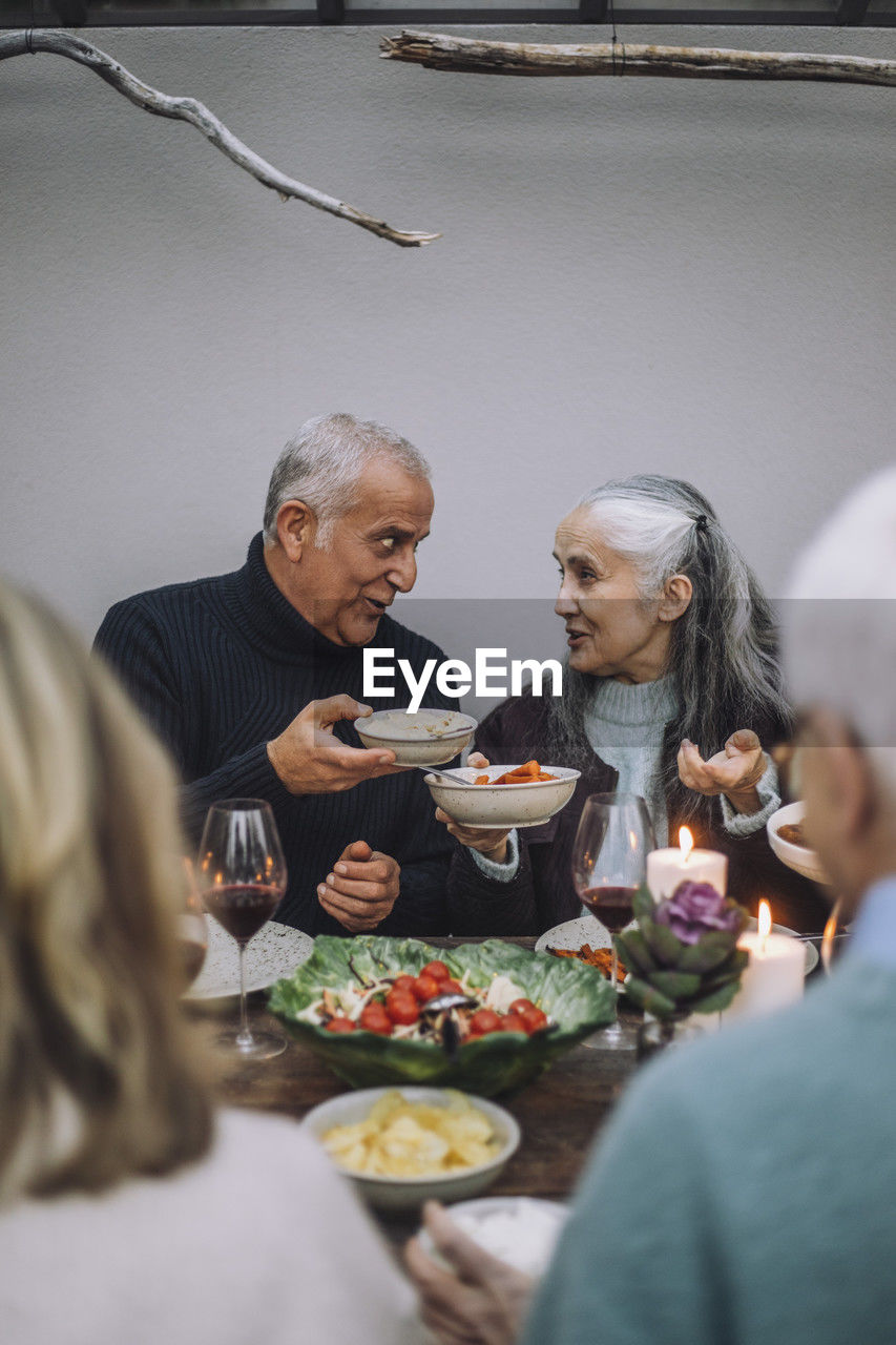 Male and female friends holding food bowls while talking at dinner party