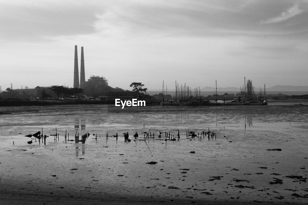 View of birds in sea against cloudy sky with power station