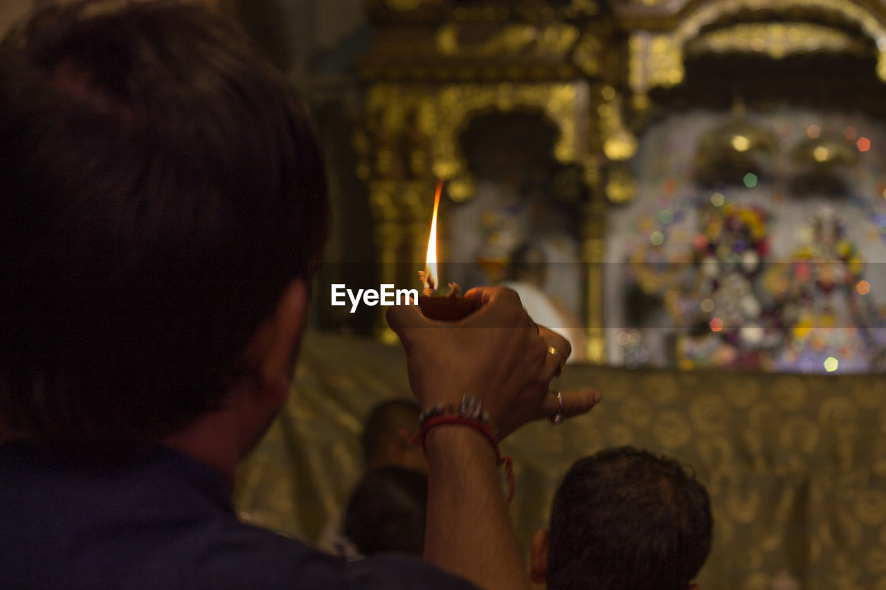 Rear view of man holding lit diya against idols in temple