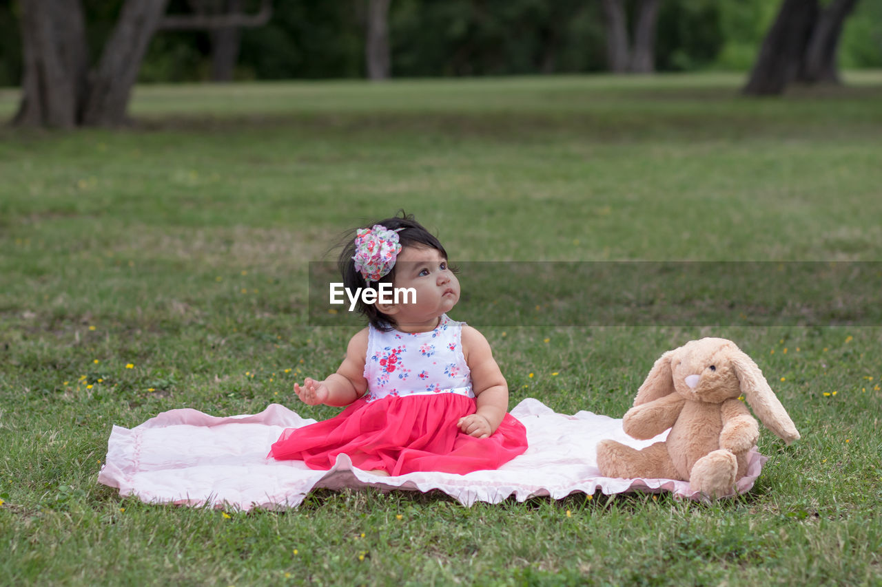Cute baby girl looking away while sitting on picnic blanket in park