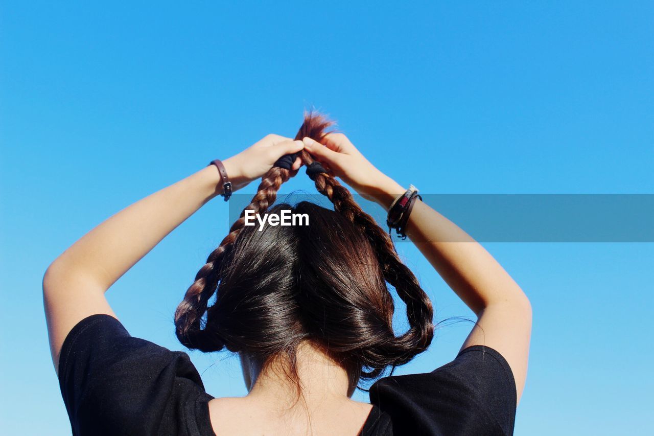 Woman holding braided hair up against clear sky