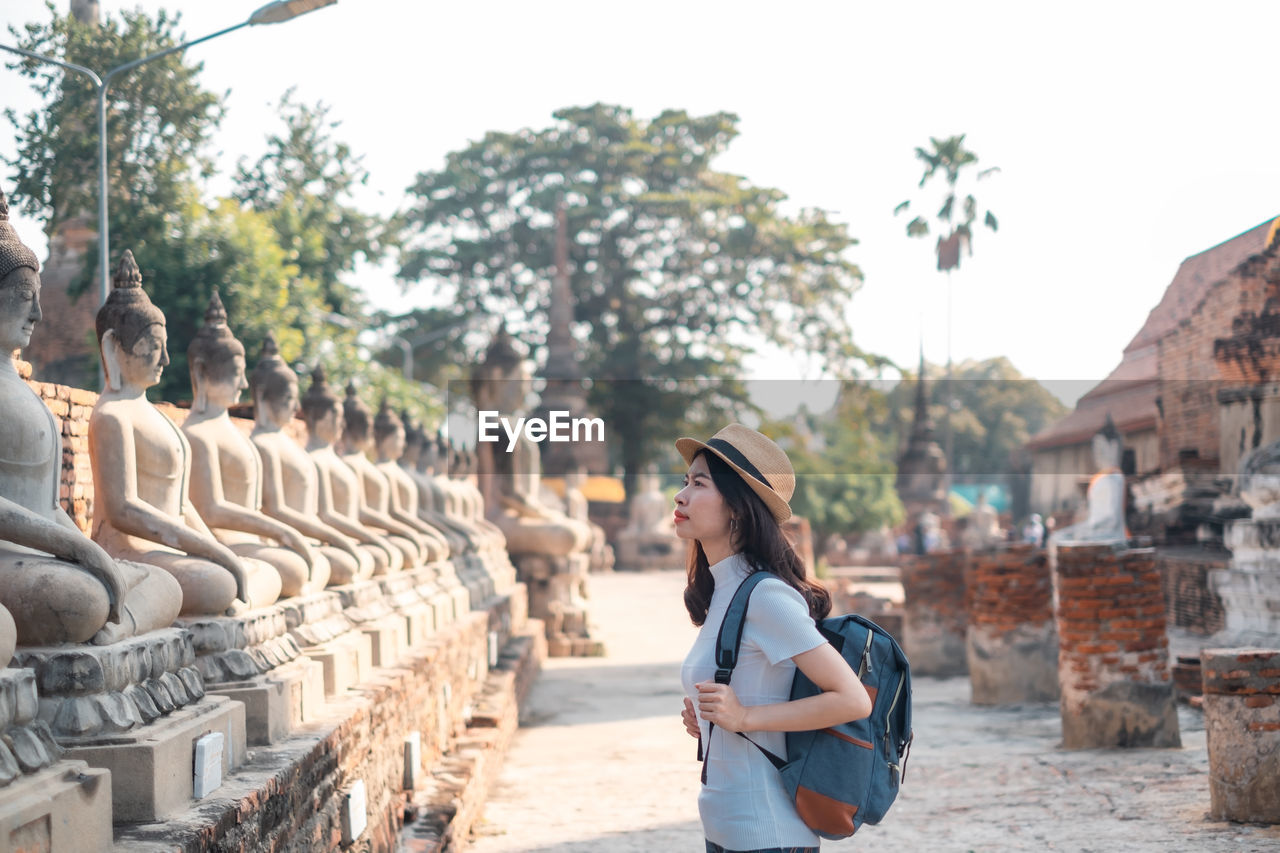 Side view of woman standing by statues in temple