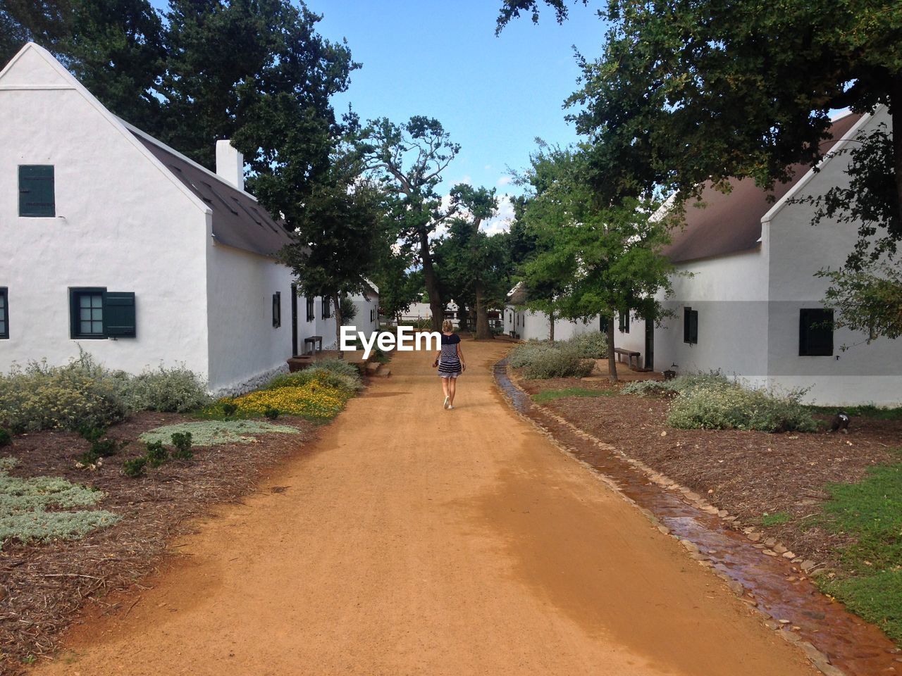 Rear view of woman walking on country road amidst houses