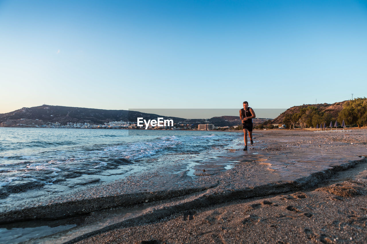 Man is jogging on jogging the beach against clear blue sky in the early morning