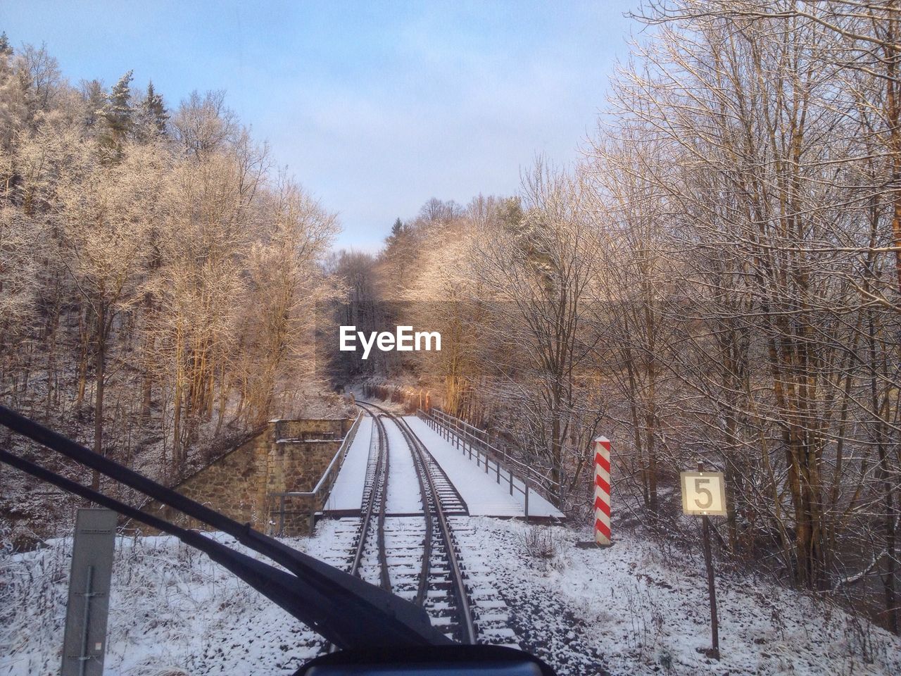 Snow covered railway tracks amidst bare trees against sky