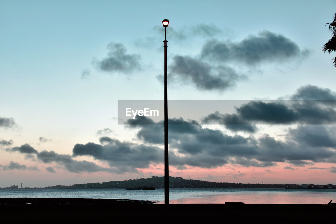 SILHOUETTE STREET LIGHT BY SEA AGAINST SKY