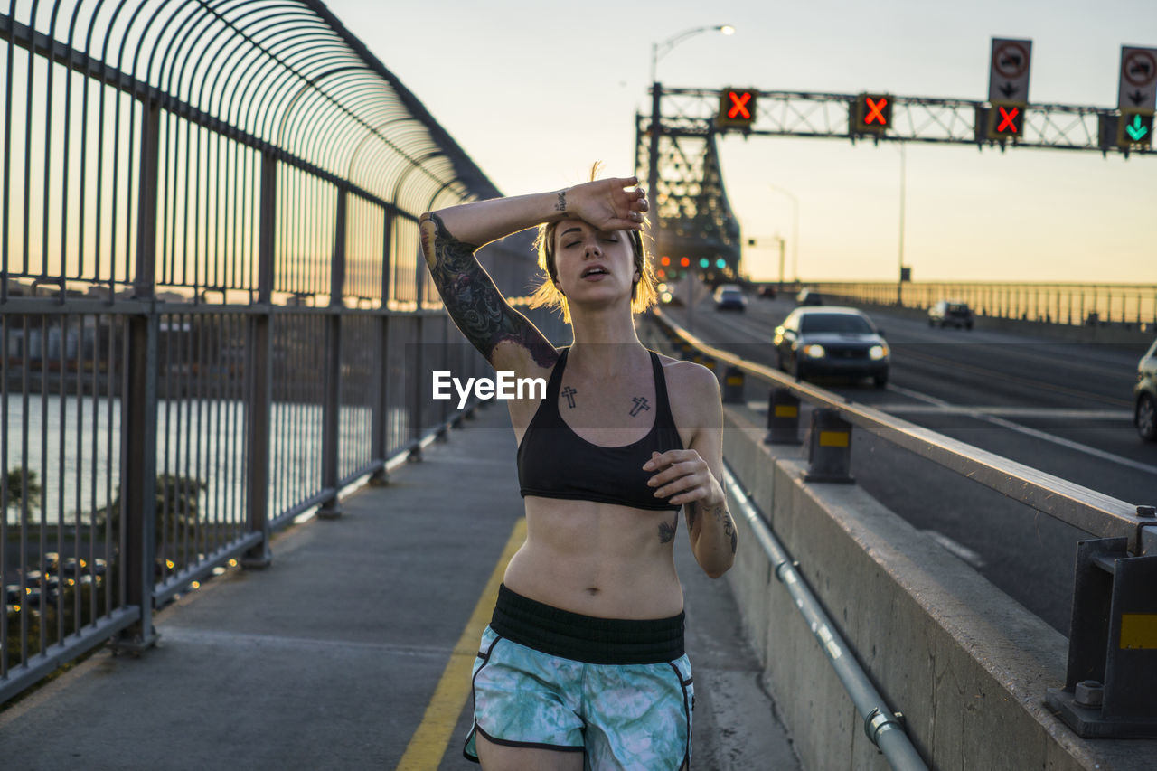 Young tattooed woman running on bridge with sunset behind