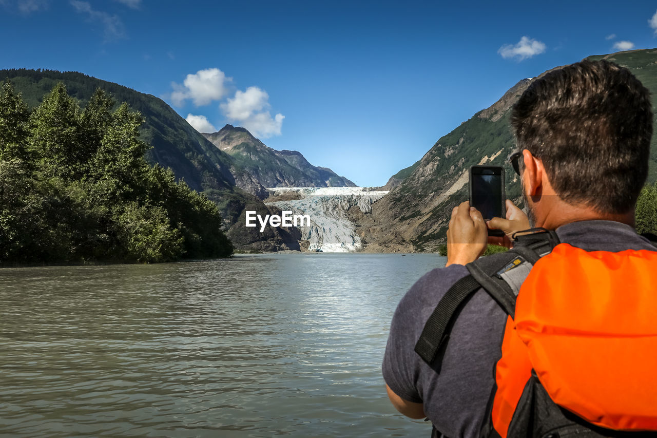 Rear view of man photographing mountains through mobile phone