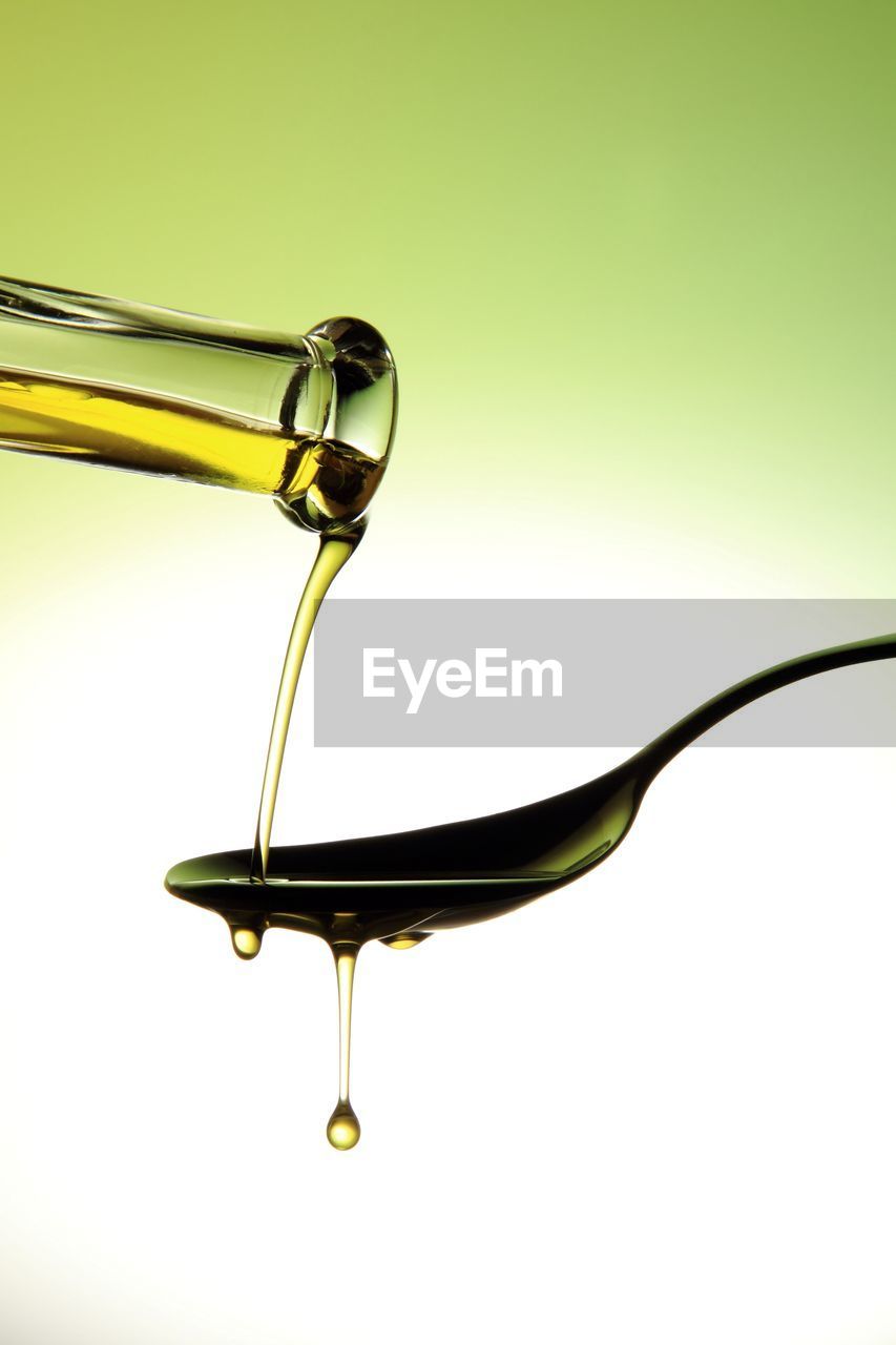 Cropped image of bottle pouring cooking oil on spoon against colored background