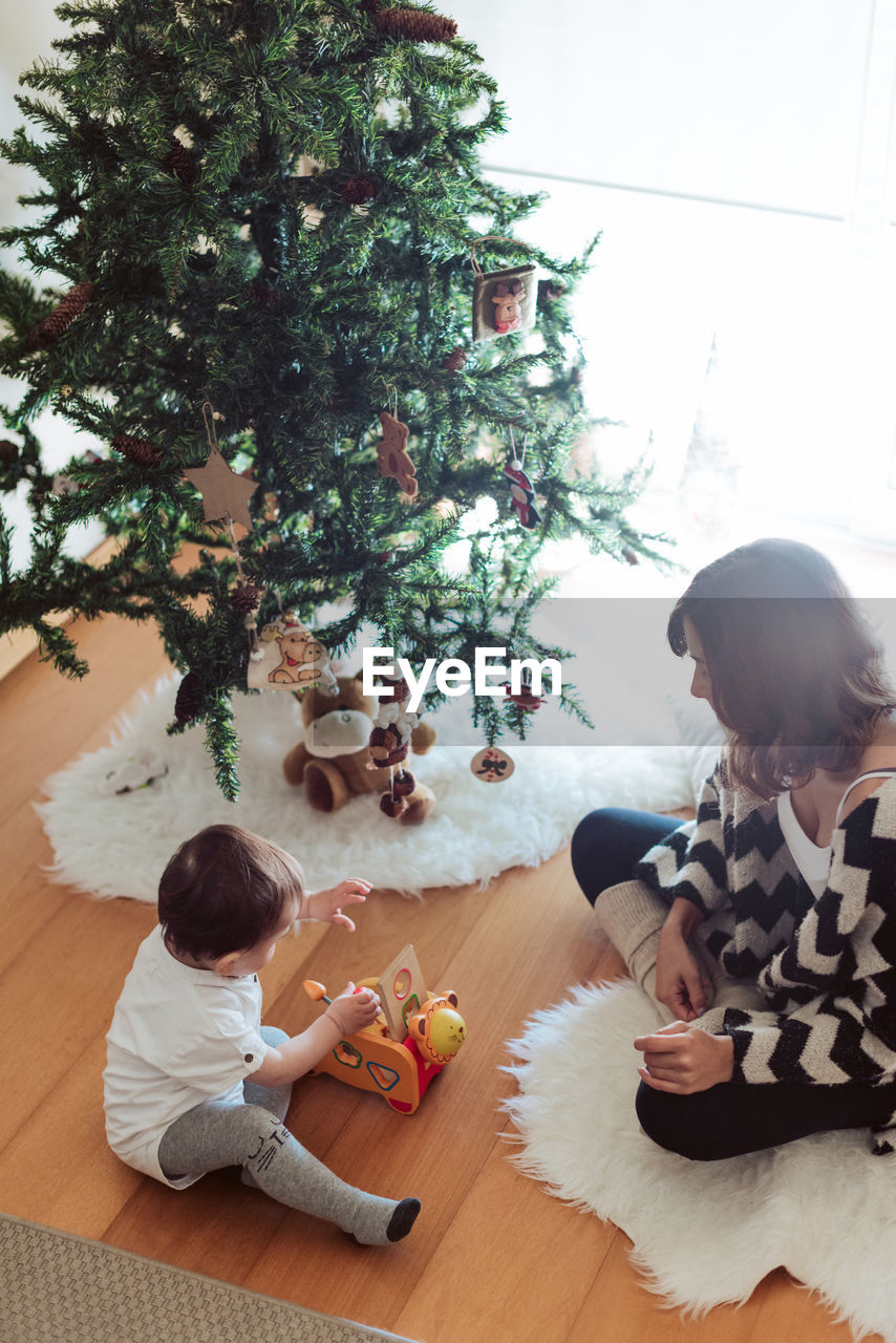 Mother and son spending leisure time by christmas tree at home