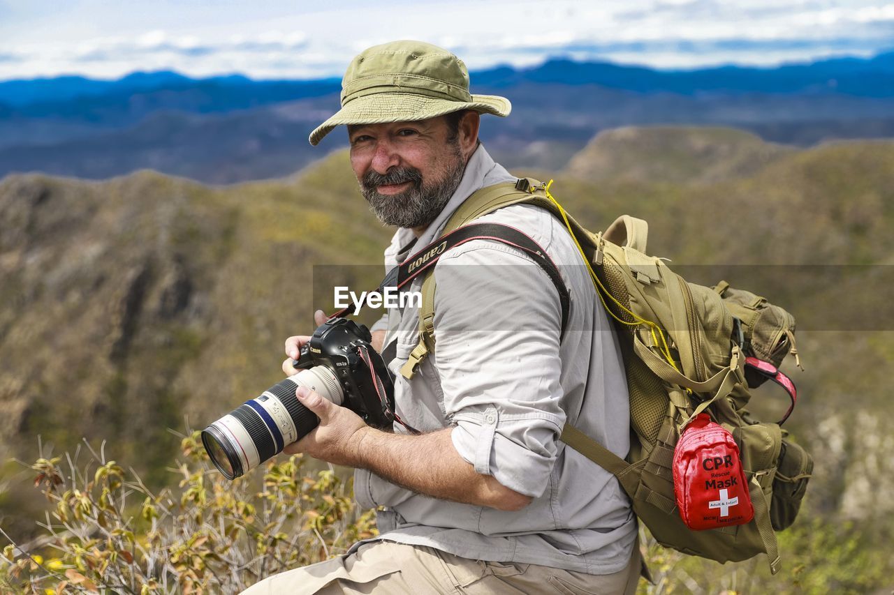 MIDSECTION OF MAN PHOTOGRAPHING AGAINST MOUNTAIN