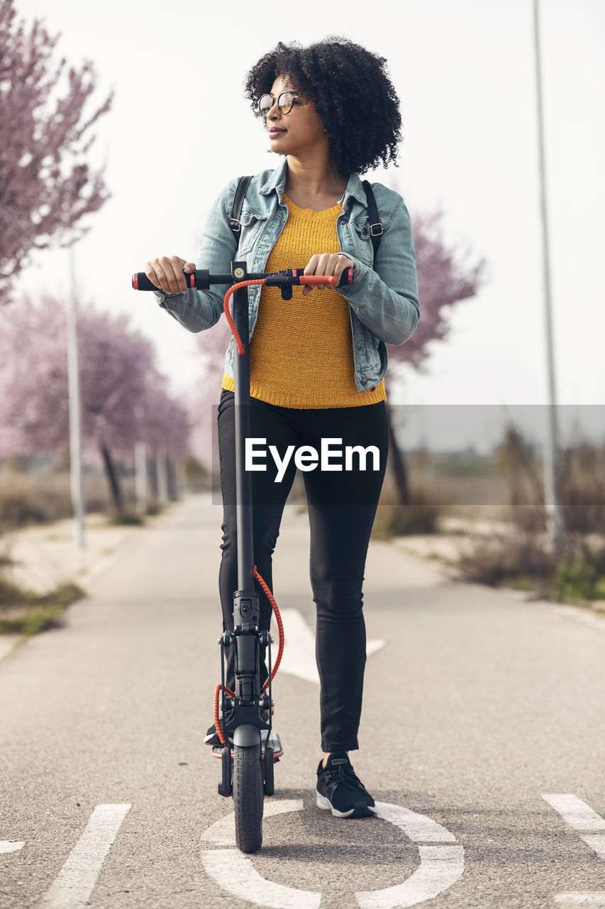 Woman looking away while standing with electric push scooter on road