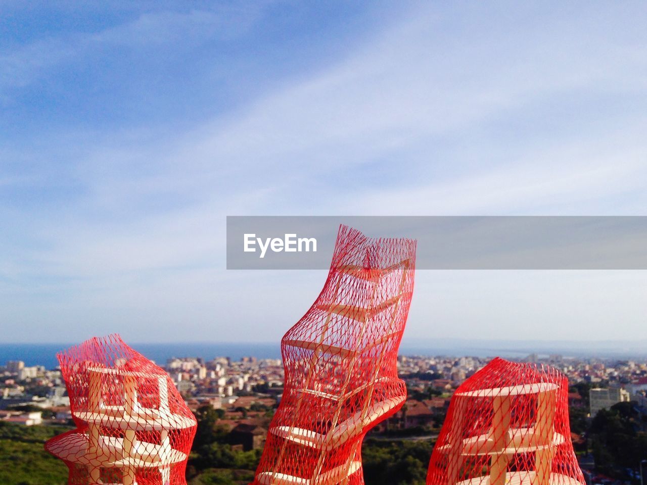 Artwork covered with red net by city against sky