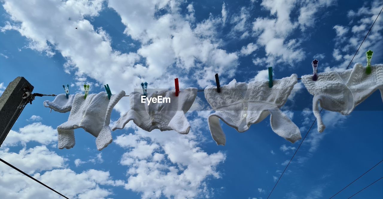 LOW ANGLE VIEW OF CLOTHES HANGING AGAINST BLUE SKY
