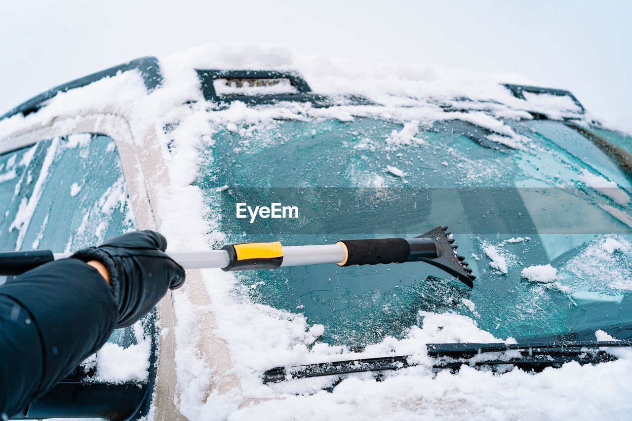 Man clearing snow off the windshield of the car in a winter day