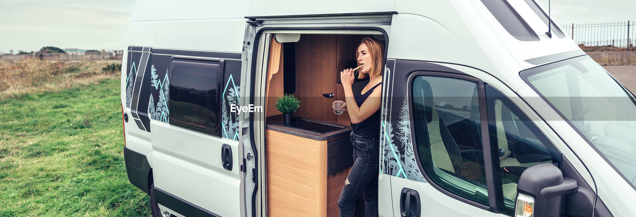 Woman brushing teeth in the morning at the door of her campervan