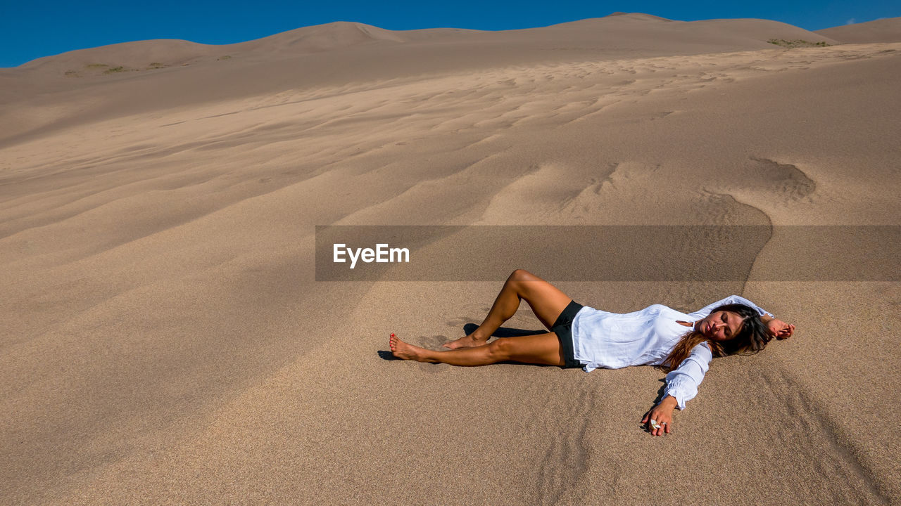 Full length of young woman lying on sand at desert