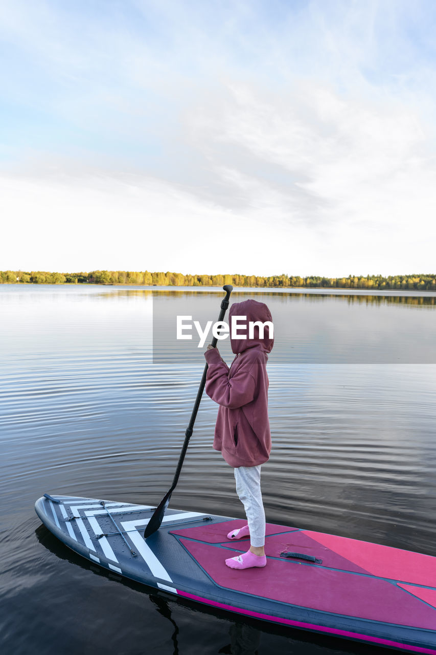 Girl wearing hooded shirt on paddleboard in lake