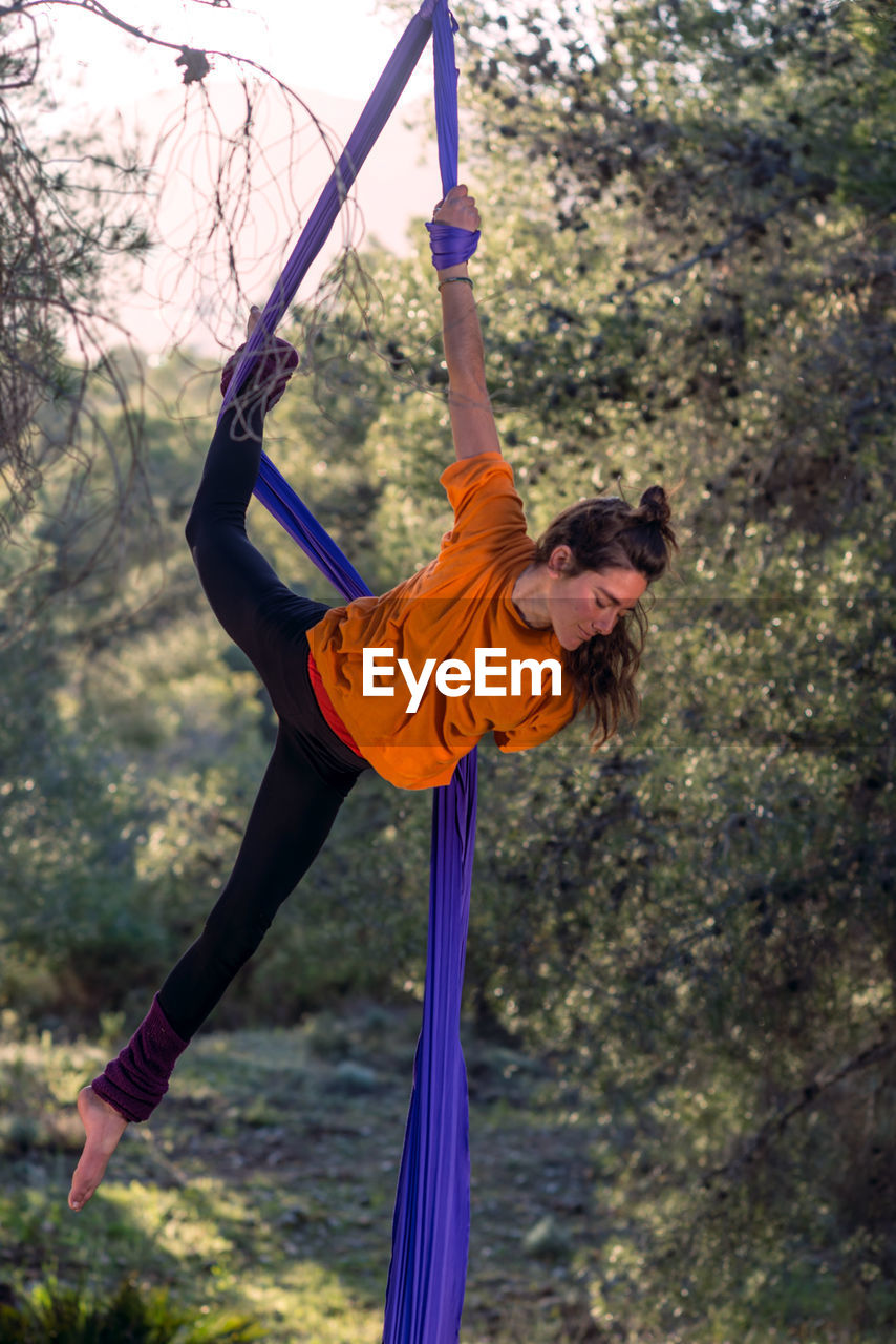 Young girl acrobat. practicing aerial silks. woman doing circus stunts with clothes in the forest. figured head position.