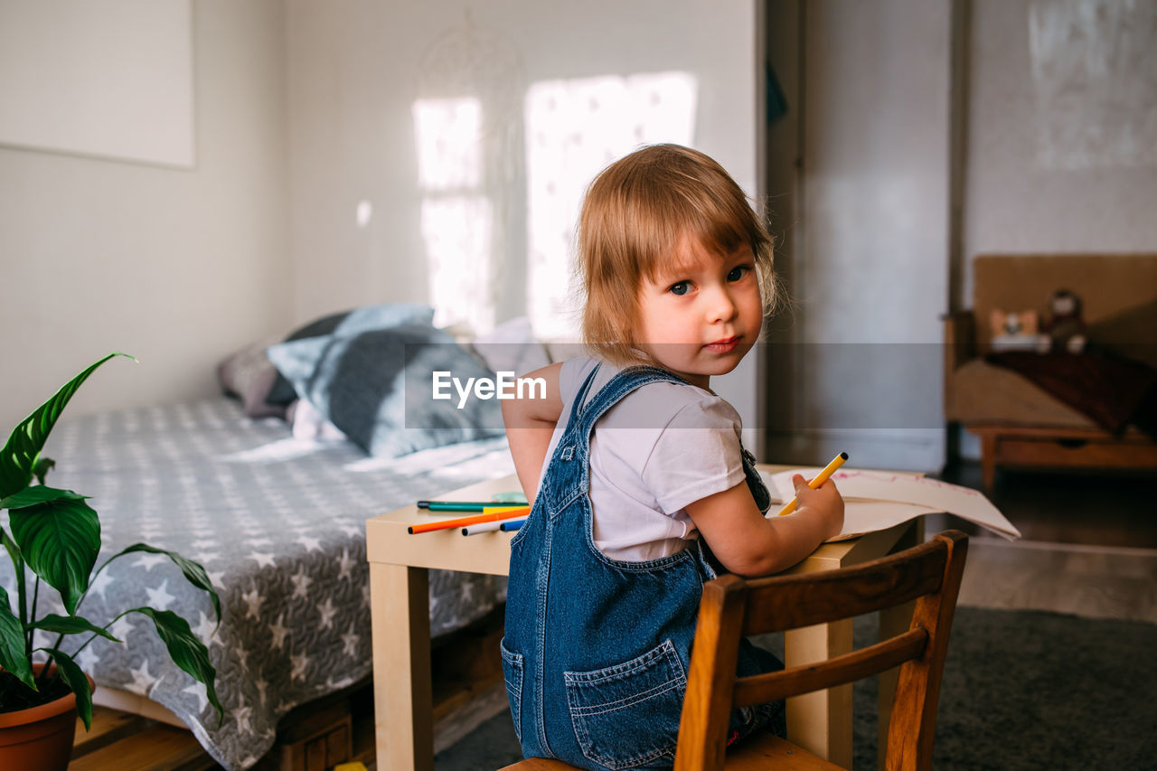 Small child at home at the children's table draws with felt-tip pens.