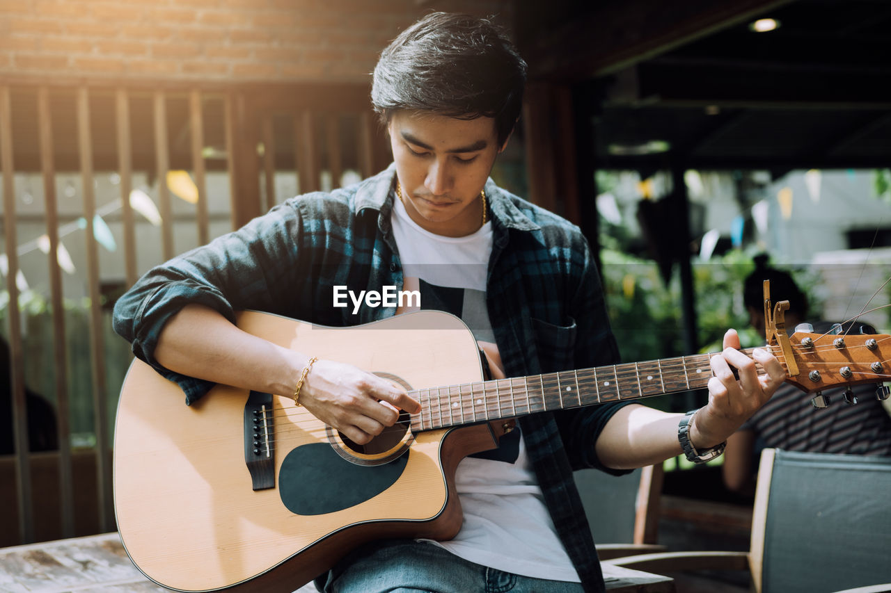 Young man playing guitar while sitting on table at outdoor restaurant