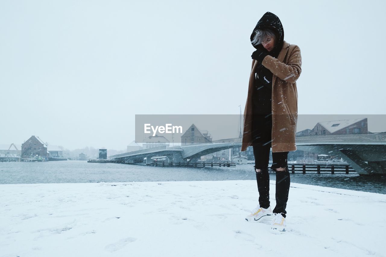 Woman standing against bridge over river in city during snowfall